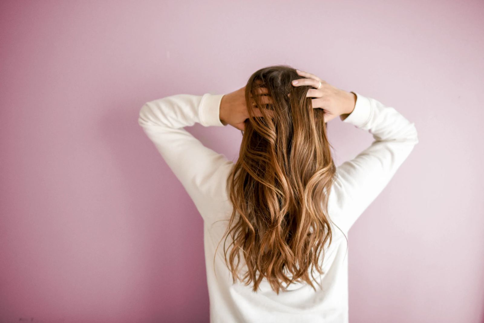 Femme de dos aux longs cheveux châtains ondulés avec balayage.